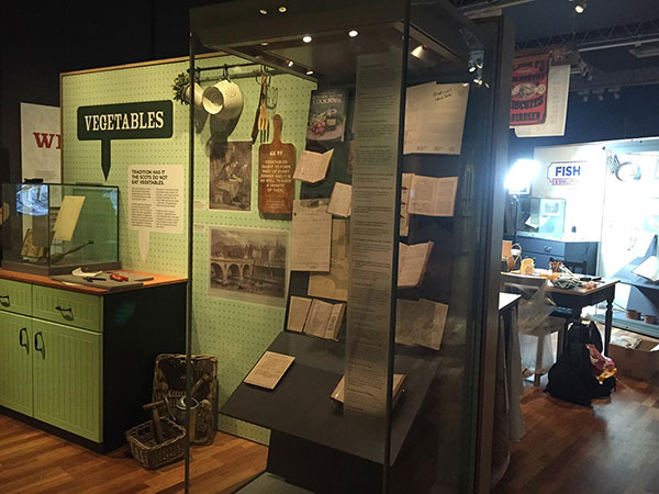 exhibition display with display cases, cupboard, papers and vegetables sign in view