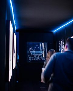 people walking down a dark corridor with led lighting with adidas branding