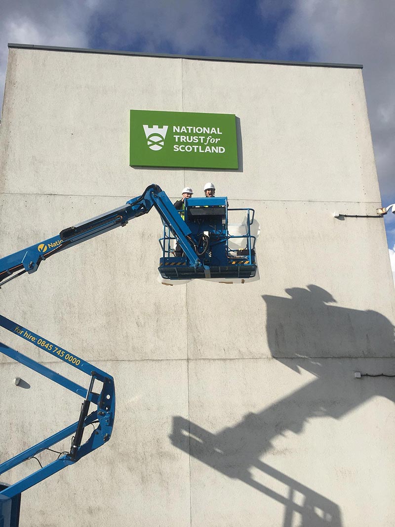 national trust for scotland sign high up and a crane with 2 technicians in front of it 