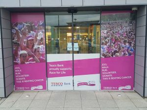 outside tesco bank with signage for beating cancer on the glass and doors