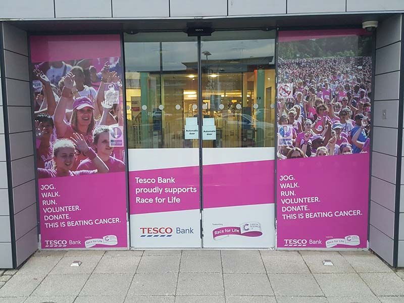 outside tesco bank with signage for beating cancer on the glass and doors