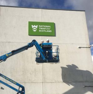 2 men up a cherry picker with national trust scotland sign in background